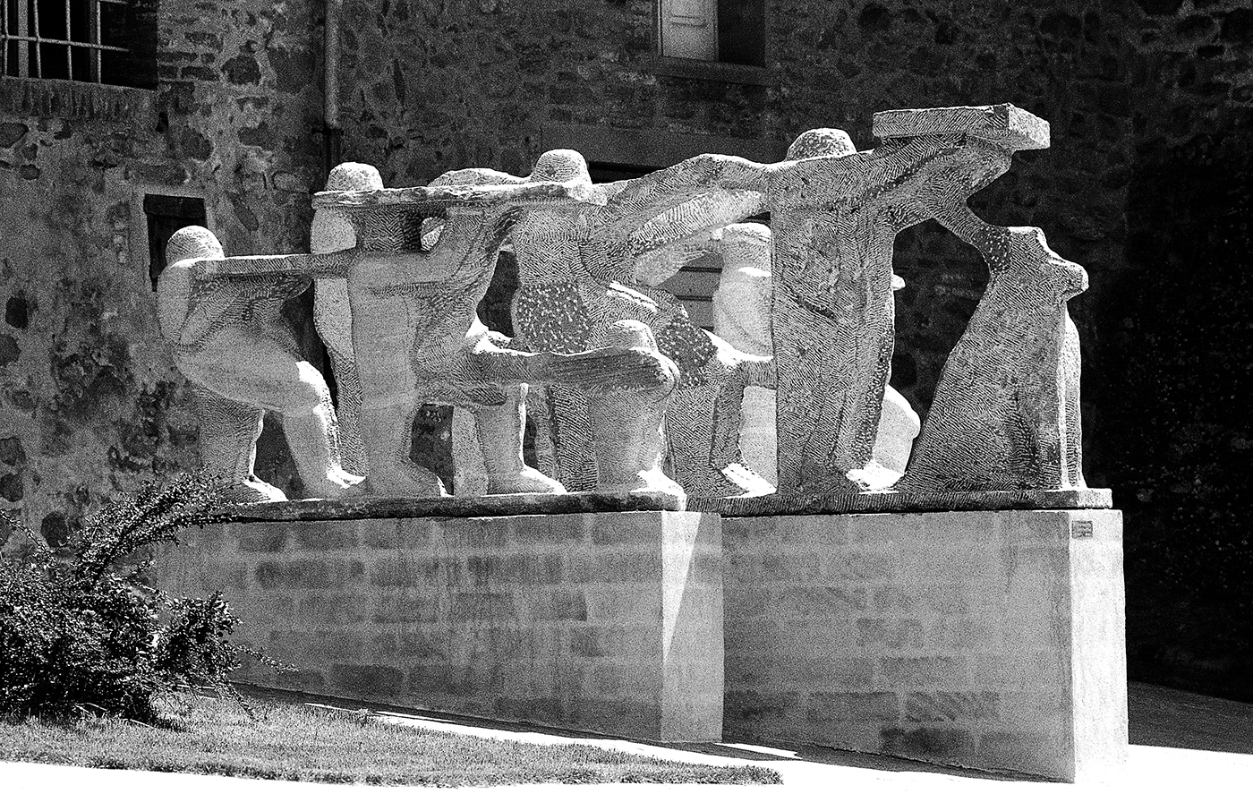 Gruppo di tre sculture in marmo che rappresentano una famiglia di aborigeni con il loro dingo in marcia in un allestimento ai pedi delle mura storiche della città di Paciano in provincia di Perugia