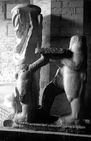 Una scultura figurativa in marmo che contiene due piccole figure di cui una regge una base esposta nello spazio dei Voltoni del palazzo Comunale di Todi in provincia di Perugia