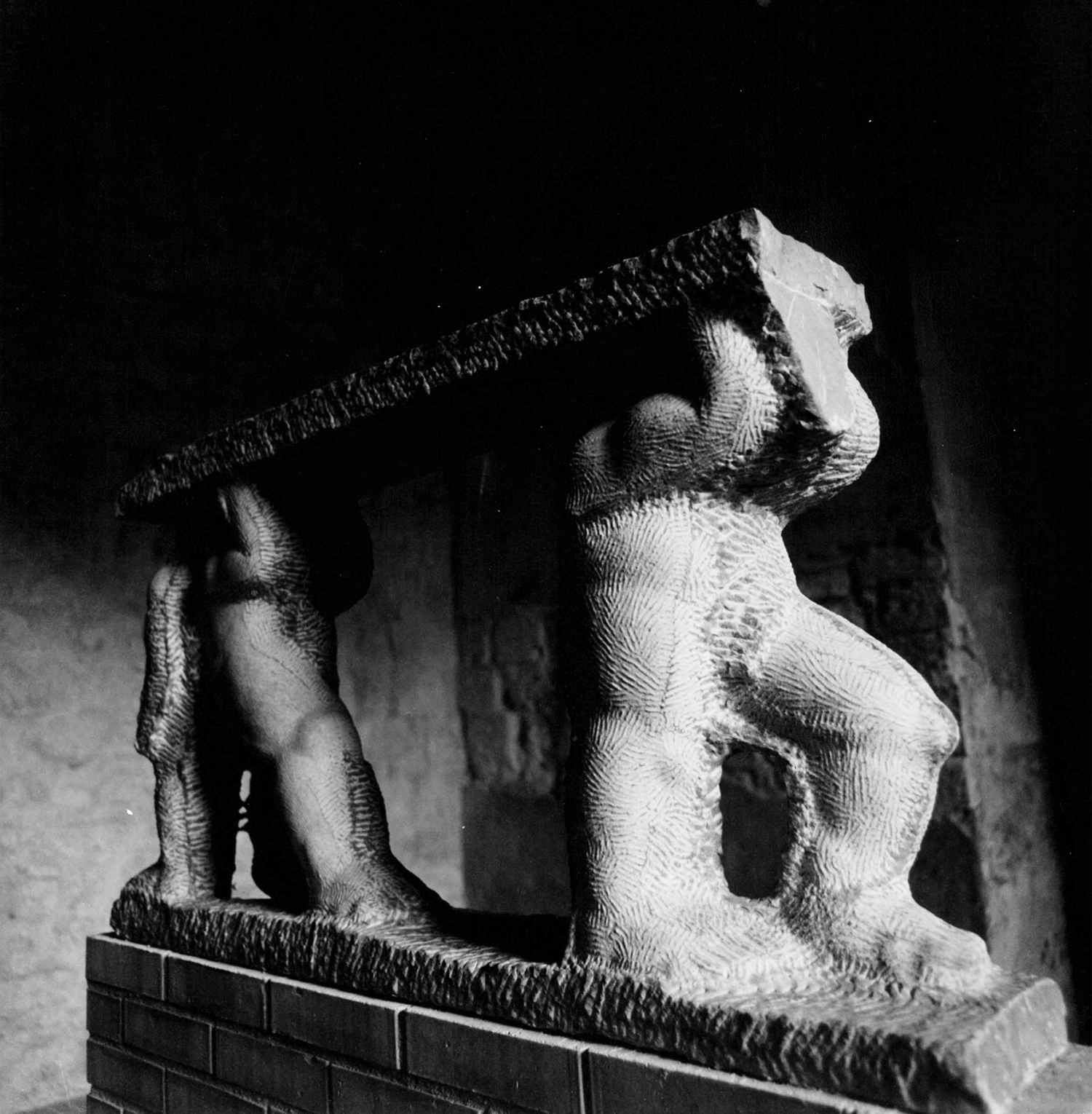 Una scultura figurativa in marmo che contiene tre piccole figure che reggono una base esposta nello spazio dei Voltoni del palazzo Comunale di Todi in provincia di Perugia