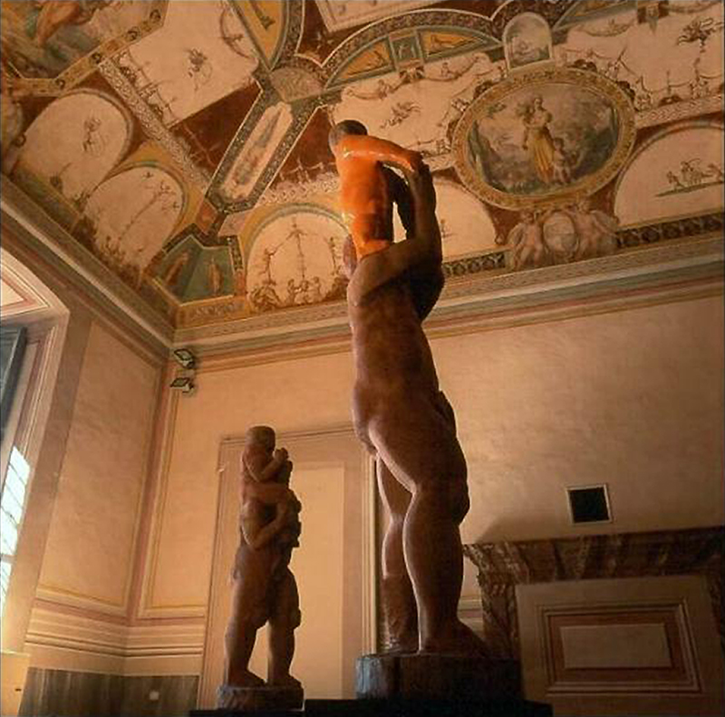 Due sculture figurative in legno ciascuna rappresenta una piccola figura sulle spalle dell'altra esposte nella Sala del Concerto di Palazzo della Corgna a Città della Pieve in provincia di Perugia