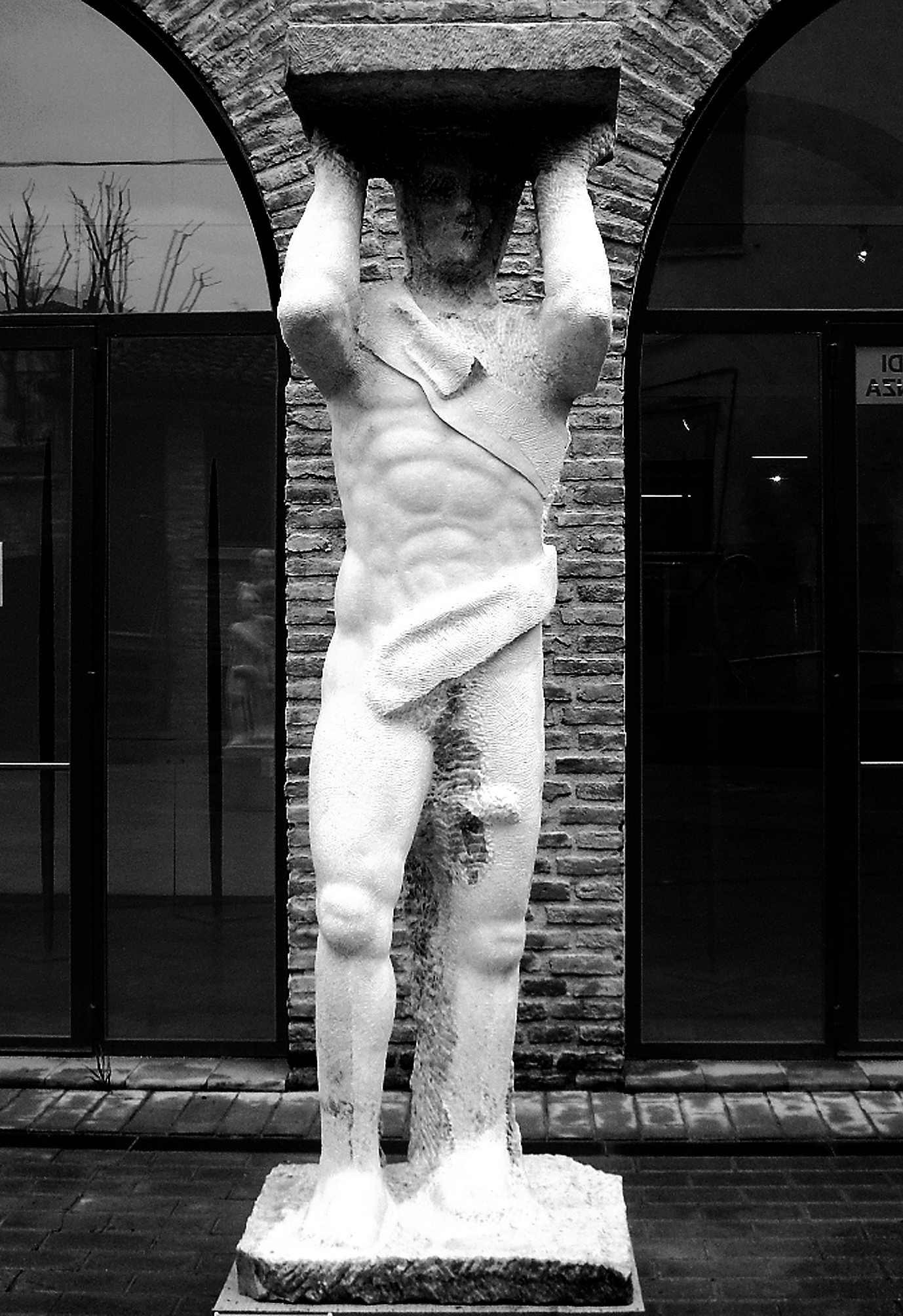 Grande scultura in marmo che rappresenta un uomo che sorregge una base al di sopra della testa